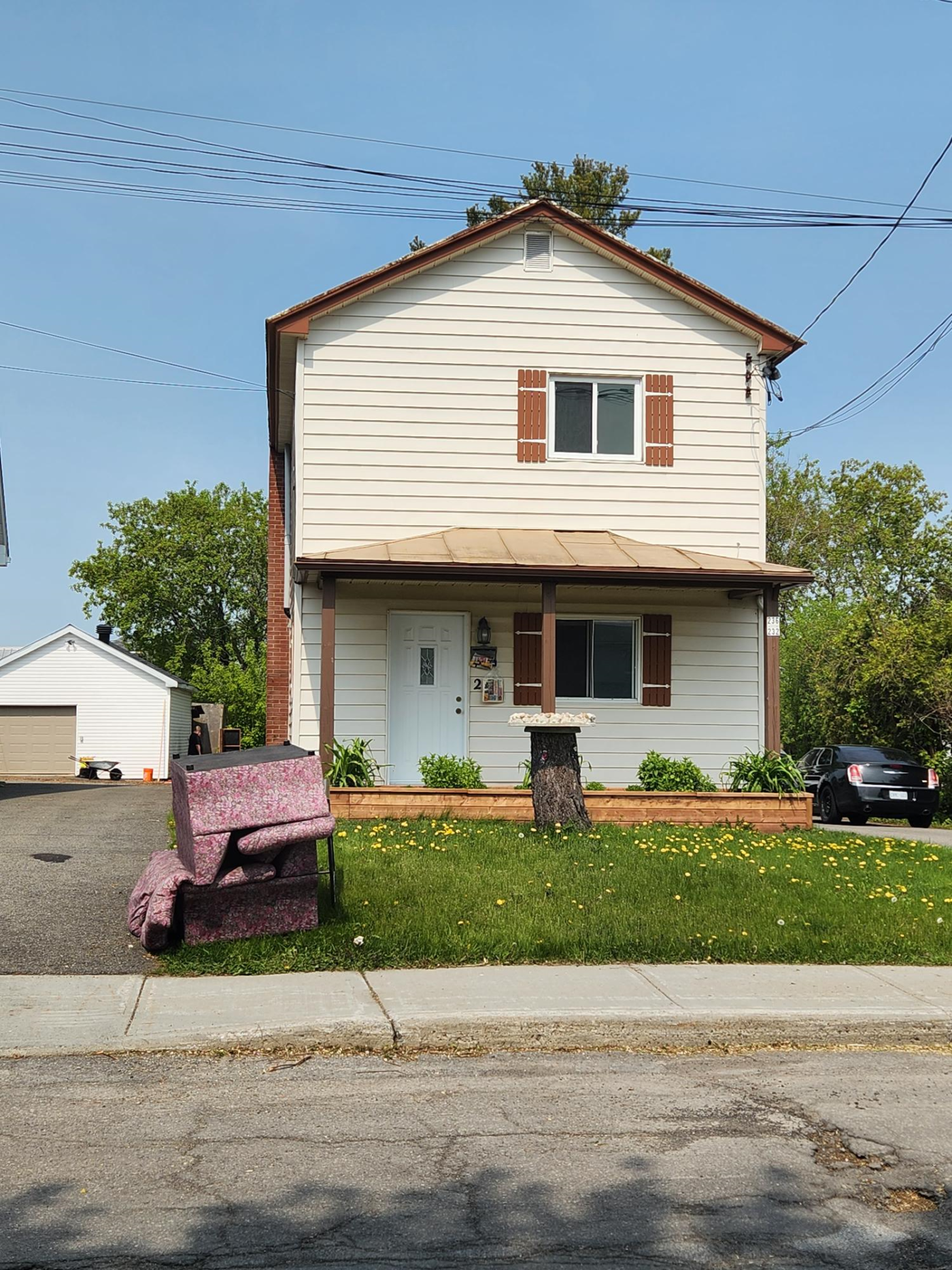 Une maison à deux étages se dresse derrière une cour d'entrée et un canapé est posé sur le trottoir.