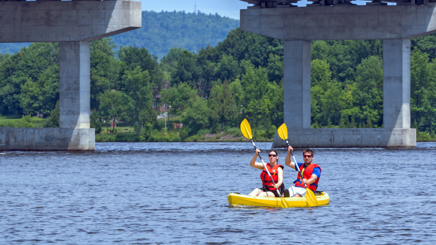 Photo of two people kayaking under a bridge.