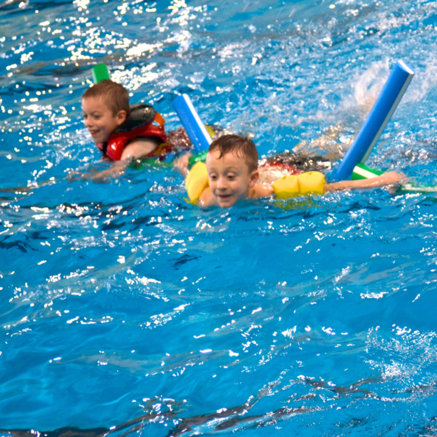 Photo of children swimming in a pool with pool noodles.