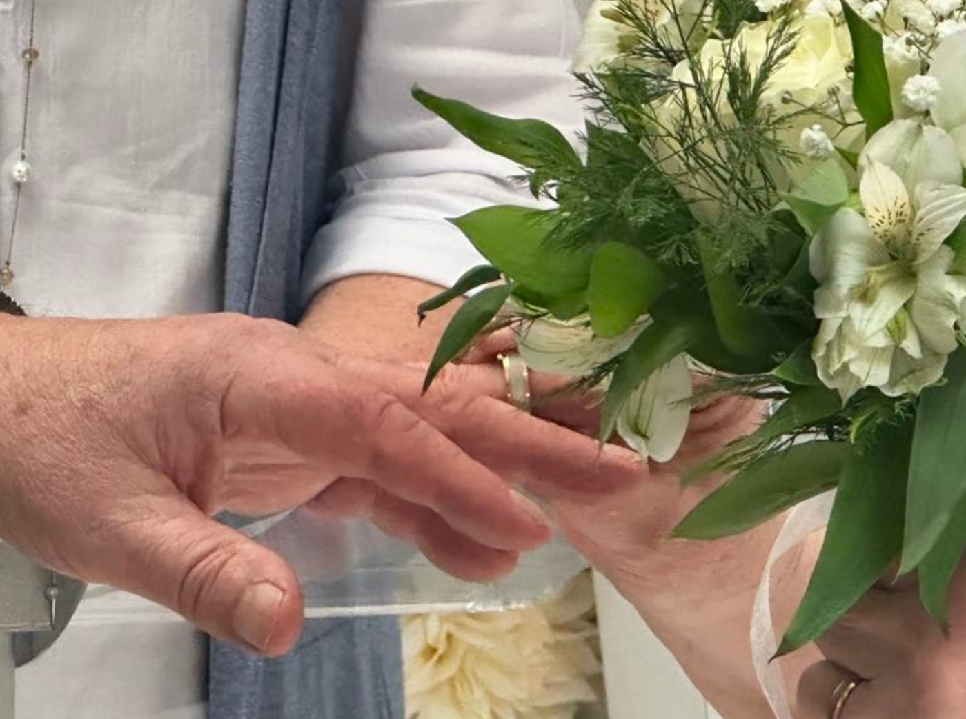 The image shows the exchange of wedding rings, accompanied by a bouquet of white flowers.