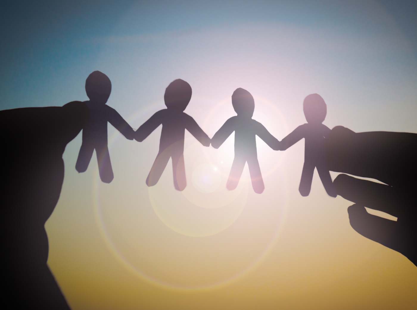 Photo of two hands holding paper cut into little people holding hands.