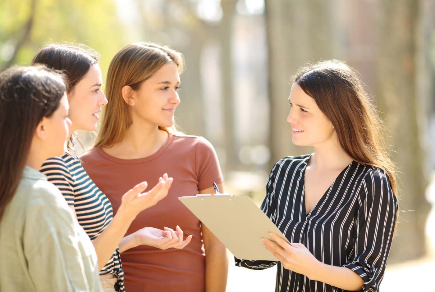 Generic photo of four people in conversation, one of whom is taking notes on a clipboard.