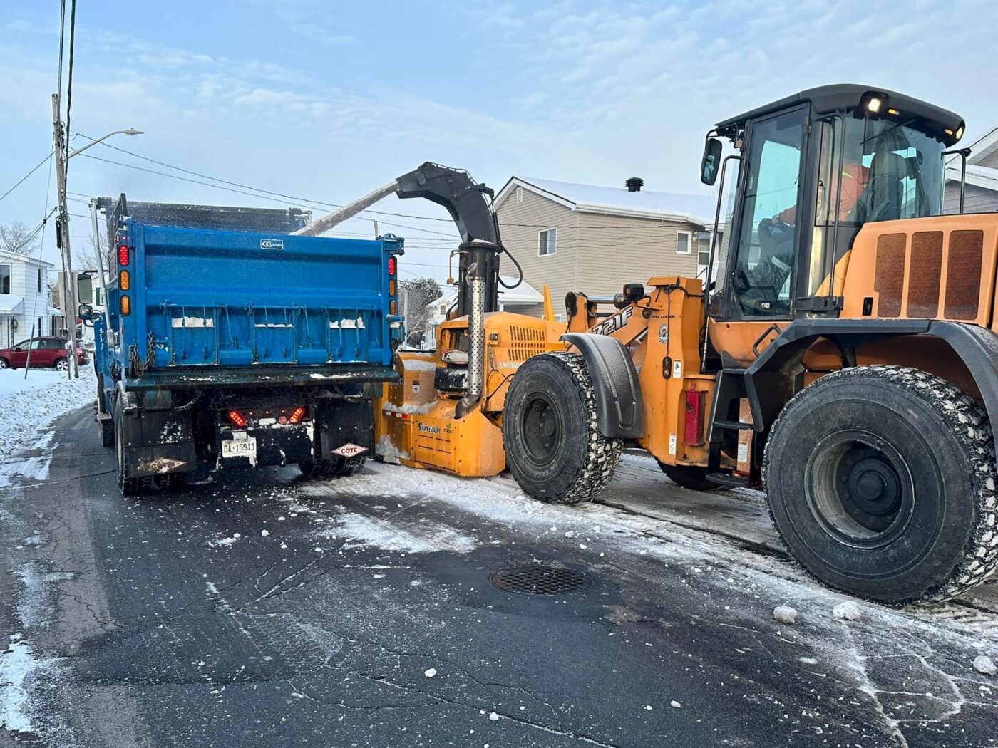 Photo of a street-clearing operation with a blower truck blowing snow into a truck for transport.