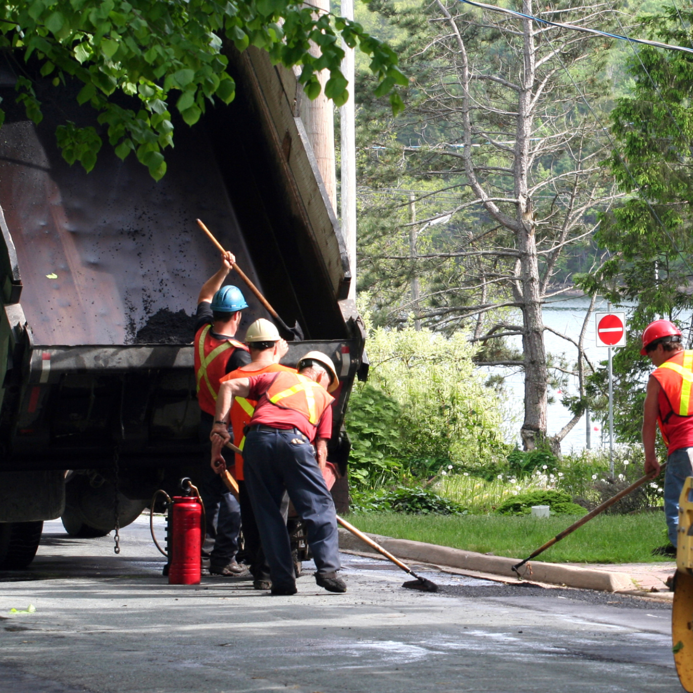 Photo of four people wearing safety vests next to a truck, repairing potholes on a street.